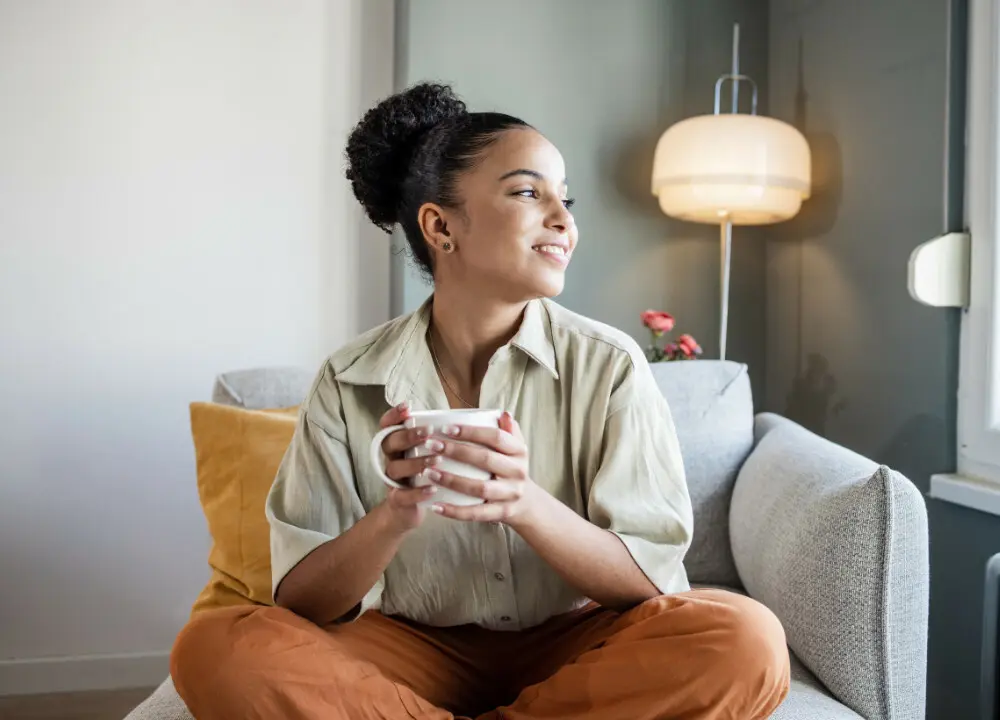 young female serviced accommodation guest looking fit and healthy sat on sofa drinking cup of tea